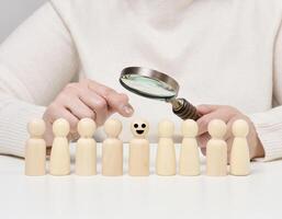 Woman holding a magnifying glass and wooden men on a white table. Personnel recruitment concept photo