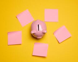 Pink ceramic piggy bank and paper stickers on a yellow background photo