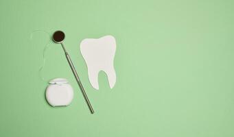 Dental floss and paper teeth on green background, oral hygiene photo