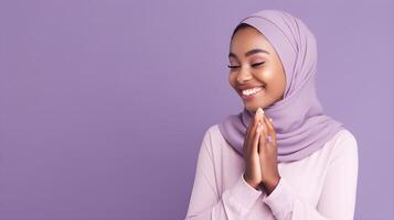 African woman wearing scarf is praying and smiling on purple background photo