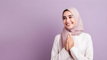 Arabic woman wearing scarf is praying and smiling on purple background photo