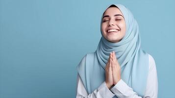 Southeast asian woman wearing scarf is praying and smiling on blue background photo