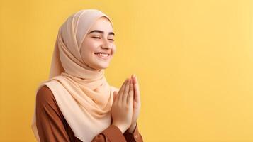 Arabic woman wearing scarf is praying and smiling on yellow background photo