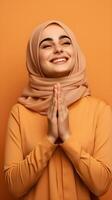 European woman wearing scarf is praying and smiling on orange background photo