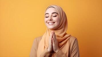 European woman wearing scarf is praying and smiling on orange background photo