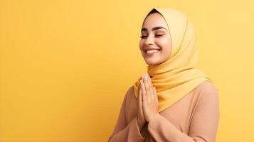 European woman wearing scarf is praying and smiling on yellow background photo
