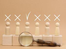 Wooden figures of men stand on a beige background and a wooden magnifying glass. photo