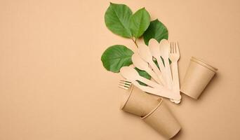 Paper cups, wooden spoons and forks on a beige background photo