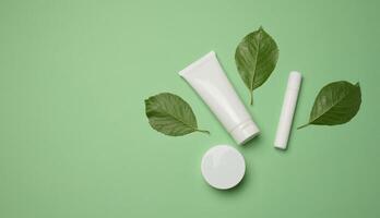 White plastic tubes, jars, and containers for cosmetic products on a green background photo