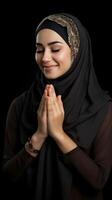 Arabic woman wearing scarf is praying and smiling on black background photo