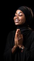 African woman wearing scarf is praying and smiling on black background photo