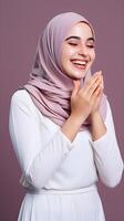 Arabic woman wearing scarf is praying and smiling on purple background photo