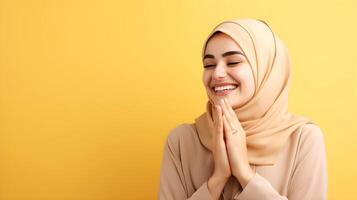 Arabic woman wearing scarf is praying and smiling on yellow background photo