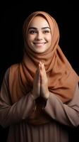 Arabic woman wearing scarf is praying and smiling on black background photo