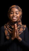 African woman wearing scarf is praying and smiling on black background photo