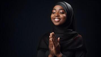 African woman wearing scarf is praying and smiling on black background photo