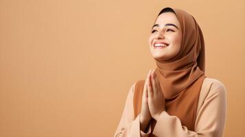Arábica mujer vistiendo bufanda es Orando y sonriente en marrón antecedentes foto