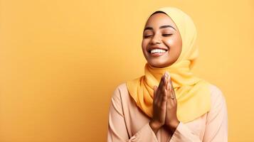 African woman wearing scarf is praying and smiling on yellow background photo