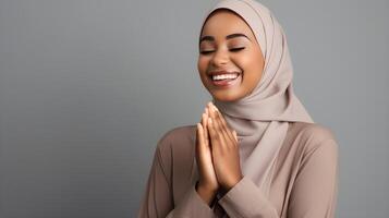 African woman wearing scarf is praying and smiling on grey background photo