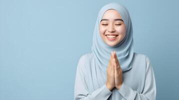 Southeast asian woman wearing scarf is praying and smiling on blue background photo