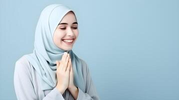 Southeast asian woman wearing scarf is praying and smiling on blue background photo