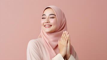 Southeast asian woman wearing scarf is praying and smiling on pink background photo