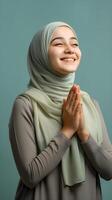 Southeast asian woman wearing scarf is praying and smiling on green background photo