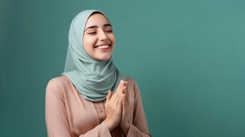 Arabic woman wearing scarf is praying and smiling on green background photo