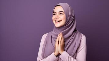 Arabic woman wearing scarf is praying and smiling on purple background photo