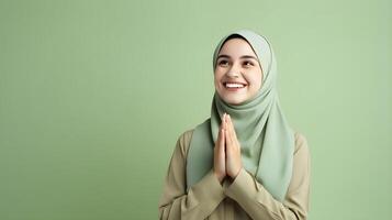 Arabic woman wearing scarf is praying and smiling on green background photo