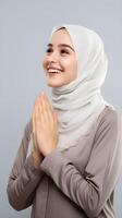 Arabic woman wearing scarf is praying and smiling on grey background photo