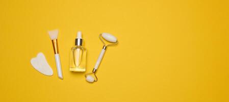 White transparent glass bottle with pipette and roller massager jade on a yellow background photo