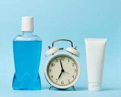 Plastic bottle with mouthwash, tube of toothpaste and round alarm clock photo