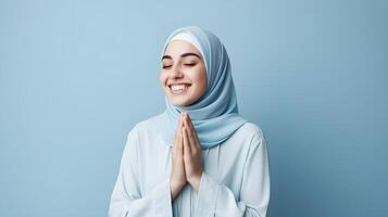 Southeast asian woman wearing scarf is praying and smiling on blue background photo