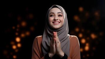 Arabic woman wearing scarf is praying and smiling on black background photo