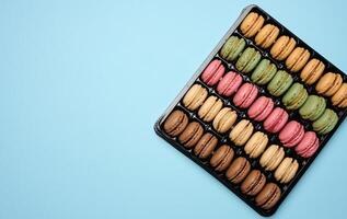 Multi-colored macarons on a blue background in a plastic box, top view photo