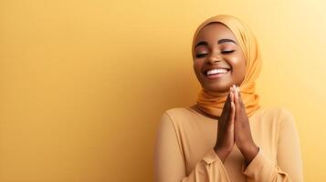 African woman wearing scarf is praying and smiling on yellow background photo