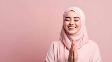 Arabic woman wearing scarf is praying and smiling on pink background photo
