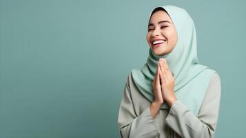 Southeast asian woman wearing scarf is praying and smiling on green background photo