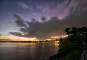 sunset over the ocean with clouds and mountains in the background photo