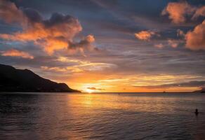 sunset over the ocean with clouds and mountains in the background photo