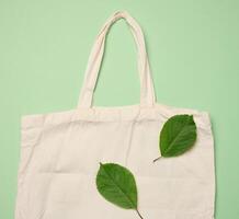 Empty beige textile bag on green background, rejection of plastic bags, flat lay photo