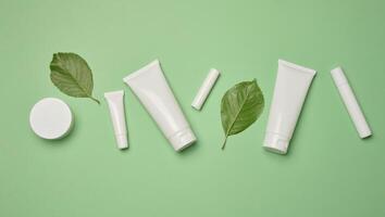 White plastic tubes, jars, and containers for cosmetic products on a green background photo