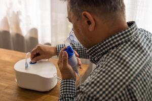 Elderly man sitting on a table and using a nebulizer mist at home photo