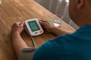 Seniory man checks blood pressure with monitor on upper arm in room photo