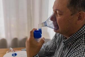 mayor hombre sentado en un mesa y utilizando un nebulizador niebla a hogar foto