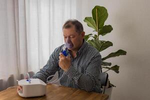 Elderly man sitting on a table and using a nebulizer mist at home photo