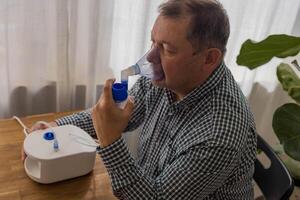 Elderly man sitting on a table and using a nebulizer mist at home photo