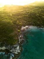 Aerial sunrise.Dark turquoise water with white foamy waves and green rocky shore photo