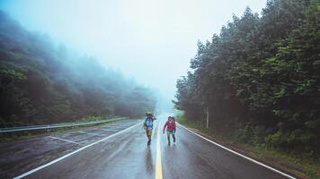 Lover asian man and asian women travel nature. Walk on the road route. traveling nature happily. Amid the mist rainy. photo